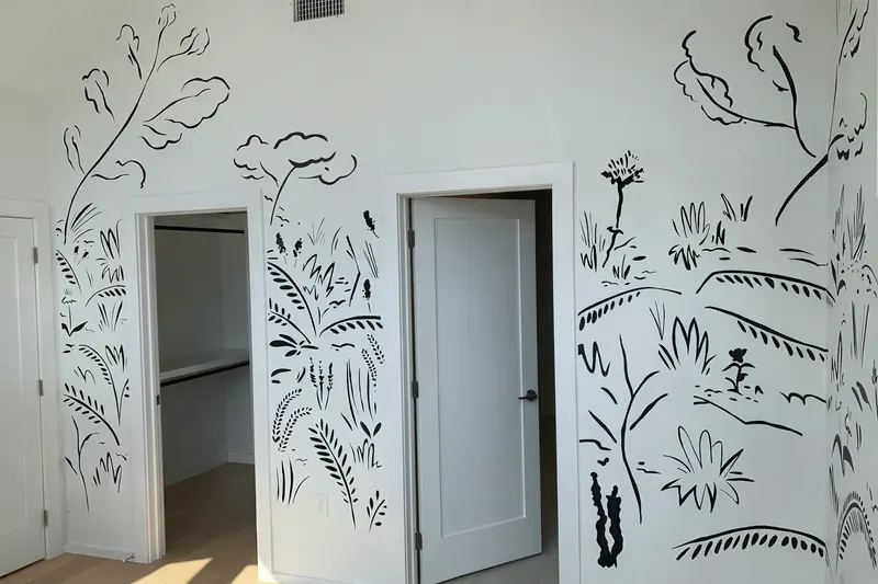Black brush-line botanical mural of leafy branches, trees and grasses painted around two doorways