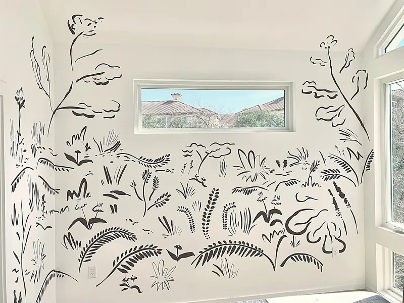 Hand-painted black brush-line mural of grasses, flowers and trees wrapping the walls of a white room around a window