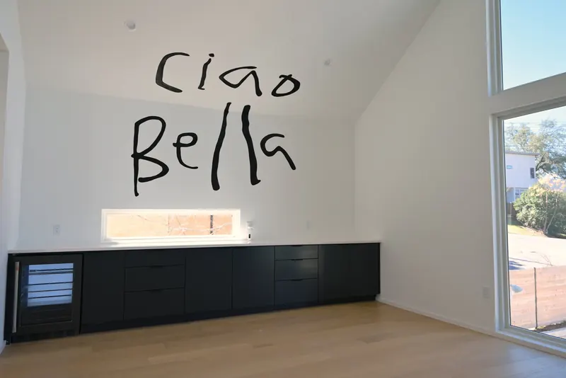 Hand-lettered "Ciao Bella" in loose black brush strokes on a white wall above a dark kitchen counter